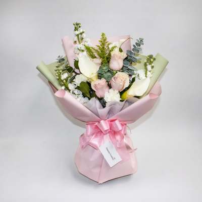 Bouquet of pale pink and white flowers wrapped in pink paper with a ribbon