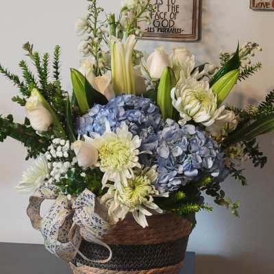 Basket arrangement with blue hydrangeas, white lilies, and pale roses