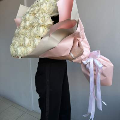 Large bouquet of white roses wrapped in pink paper with ribbon