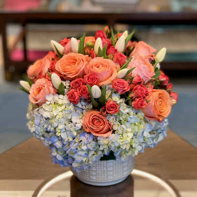 Peach and pink roses with blue hydrangeas in a white vase