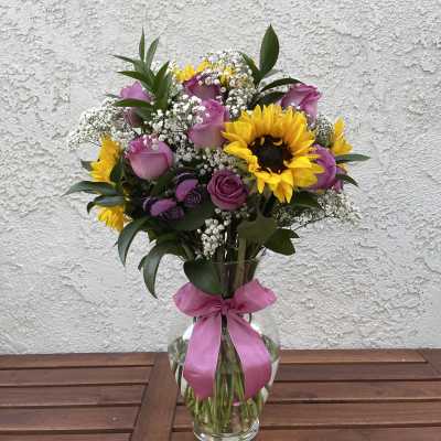Bouquet of pink roses and yellow sunflowers in a glass vase with a pink ribbon