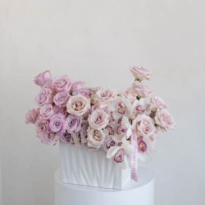 Pink roses and white orchids arranged in a white box