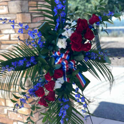 Standing floral spray with red roses, blue flowers, and ribbon