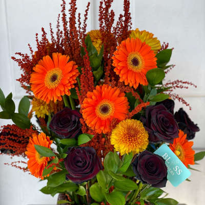 Basket arrangement with orange gerbera daisies and dark roses