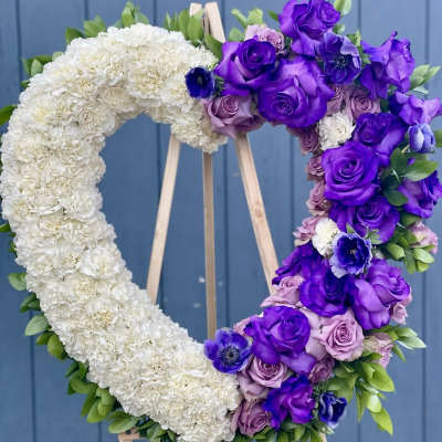 Heart-shaped floral wreath with white and purple flowers on a wooden stand