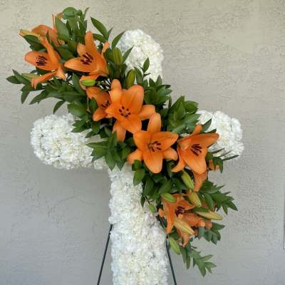 Orange lilies on a white floral cross standing on an easel
