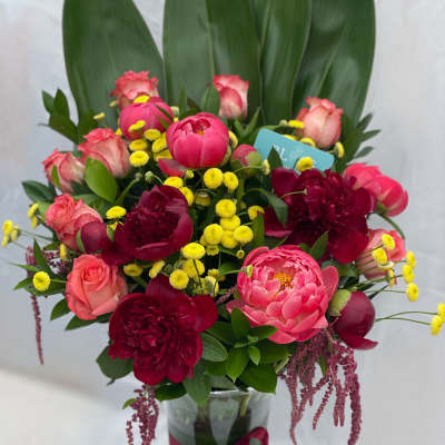 Pink and burgundy flowers arranged in a glass vase with a ribbon