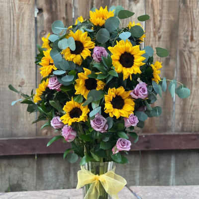 Sunflower and lavender rose bouquet in a clear vase with a yellow ribbon