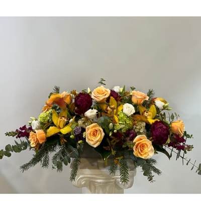 Mixed bouquet of peach roses, yellow blooms, and burgundy flowers in a vase