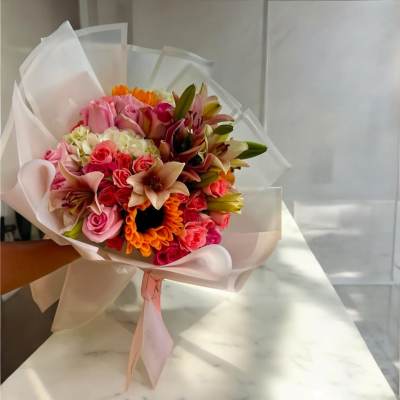 Hand-tied bouquet of pink roses, lilies, and orange flowers wrapped in white paper