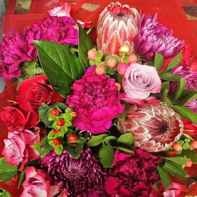 Bouquet of pink and purple flowers with red roses and green foliage