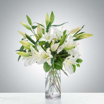 Tall arrangement of white lilies with buds in a clear glass vase