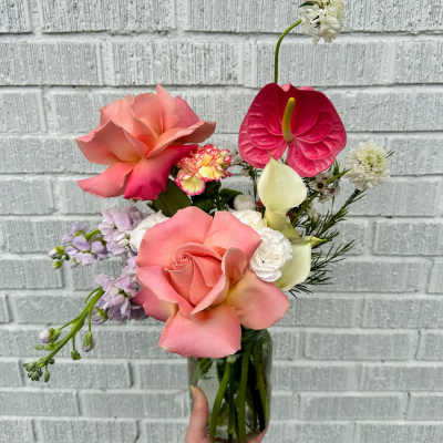 Tall mixed arrangement of peach roses, pink anthurium, white calla lilies, and other blooms in a clear glass vase.