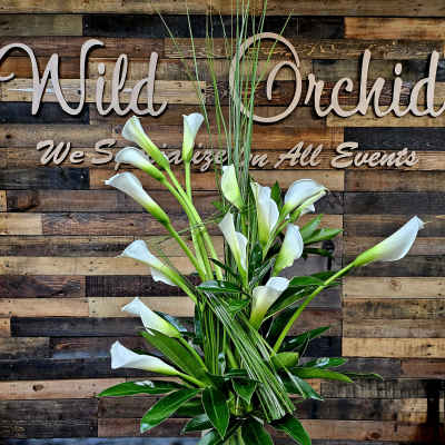 White calla lilies in a clear glass vase with tall grass accents