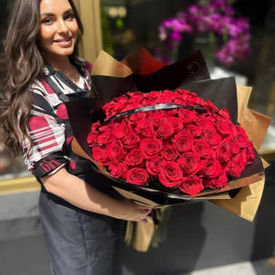 Large hand-held bouquet of tightly clustered red roses wrapped in black and tan paper