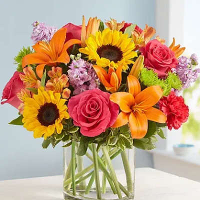Bright mixed bouquet of sunflowers, roses, lilies, and carnations in a glass vase