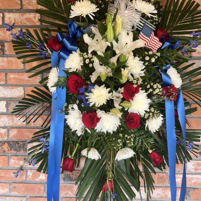 Standing floral spray with red roses, white lilies, and blue ribbons