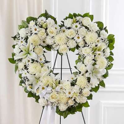 Heart-shaped white floral wreath on a black stand
