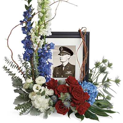 Floral tribute around a framed military portrait with red, white, and blue flowers