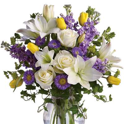 White lilies, roses, purple flowers, and yellow tulips in a glass vase