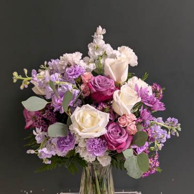 Tall mixed bouquet of white, pink, and purple flowers in a clear glass vase