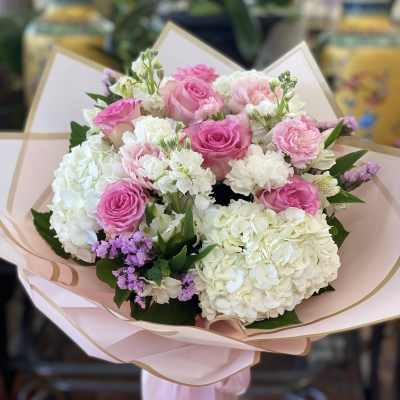 Pink and white bouquet of roses, hydrangeas, and carnations wrapped in blush paper
