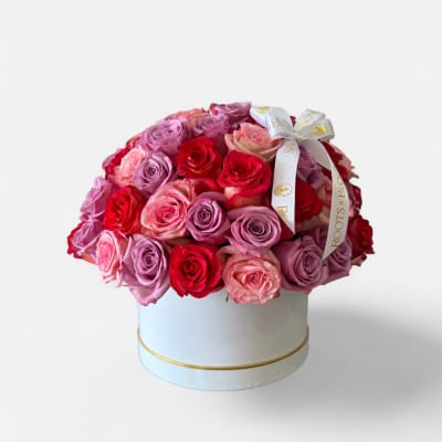 Round box arrangement of pink, lavender, and red roses with a ribbon bow
