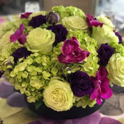 Round bouquet of pale green and purple flowers in a black container