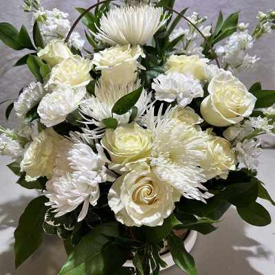 White roses and chrysanthemums arranged in a basket with greenery