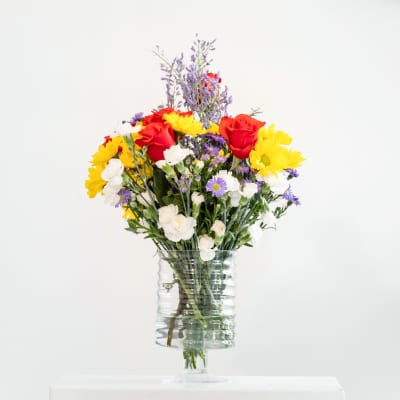 Mixed bouquet of red roses, yellow daisies, and white flowers in a clear glass vase