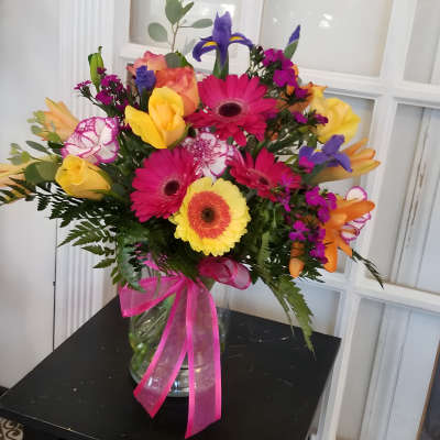 Bright mixed bouquet in a glass vase with a pink ribbon