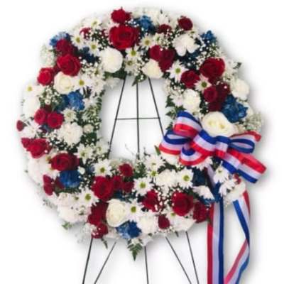 Circular floral wreath on an easel with red, white, and blue flowers and ribbon