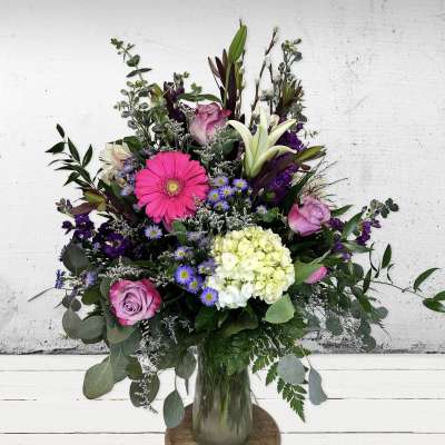 Tall mixed bouquet of pink gerbera, roses, white lilies and green hydrangea in a clear glass vase