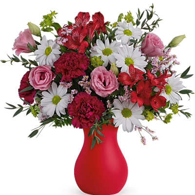 Mixed bouquet of daisies, pink blooms, and red flowers in a red vase