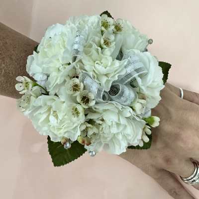 White wrist corsage with small blossoms and silver ribbon worn on a hand.