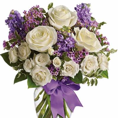 White roses and purple flowers arranged in a glass vase with a purple ribbon.
