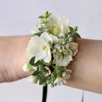 White floral wrist corsage with green accents on a wrist