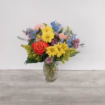 Mixed bouquet of yellow daisies, orange rose, and pastel flowers in a clear glass vase