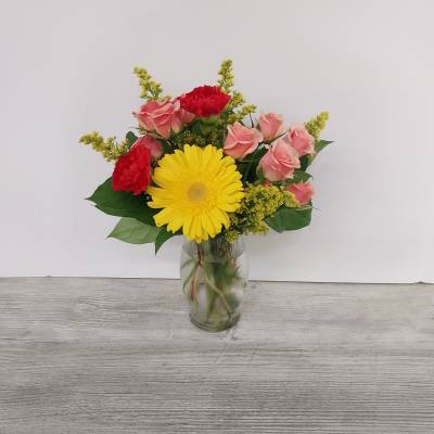 Small vase arrangement with yellow gerbera daisy, pink roses, and red carnations in a glass vase