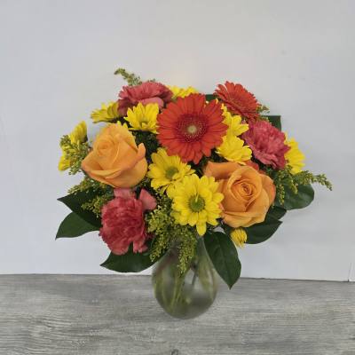 Bright bouquet of orange roses, red gerberas, yellow daisies, and carnations in a glass vase