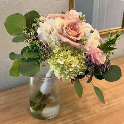 Hand-tied bouquet of pale pink roses and green and white hydrangeas in a clear glass vase