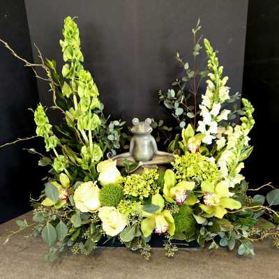 Green floral arrangement with a small frog statue in the center