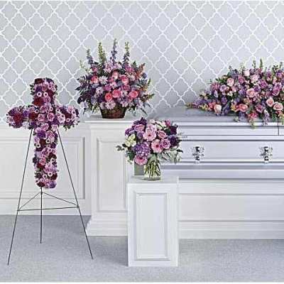 Floral casket spray and standing arrangements in pink and purple around a white casket