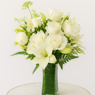 White roses and lilies arranged in a green glass vase