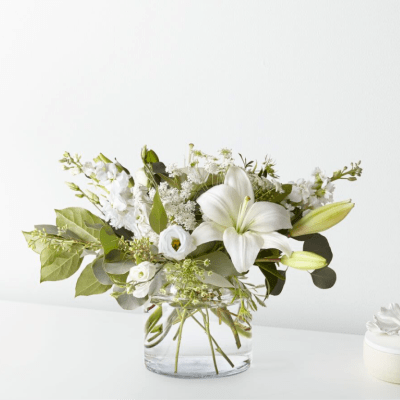 White lily and mixed white flowers in a clear glass vase