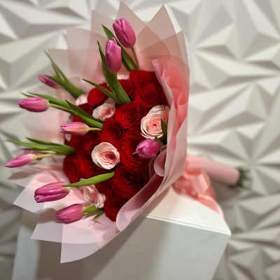 Bouquet of red roses and pink tulips wrapped in pale pink paper