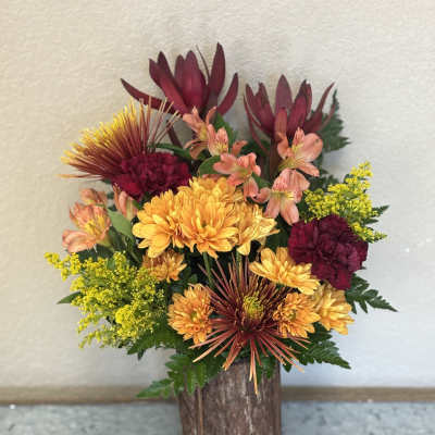 Mixed bouquet of orange, burgundy, and yellow flowers in a rustic wooden vase