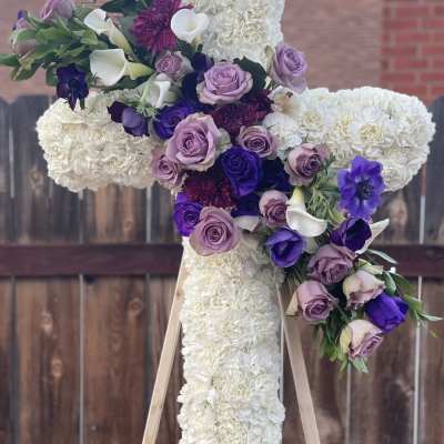 Large floral cross covered in white blooms with purple roses and calla lilies