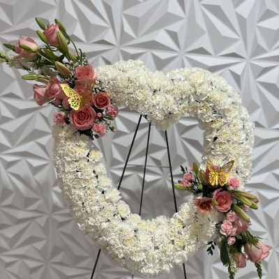 Heart-shaped white floral wreath with pink rose accents on a stand