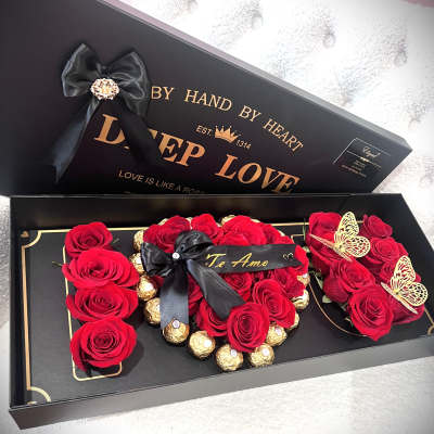 Red roses arranged in a black gift box with gold chocolates and ribbon